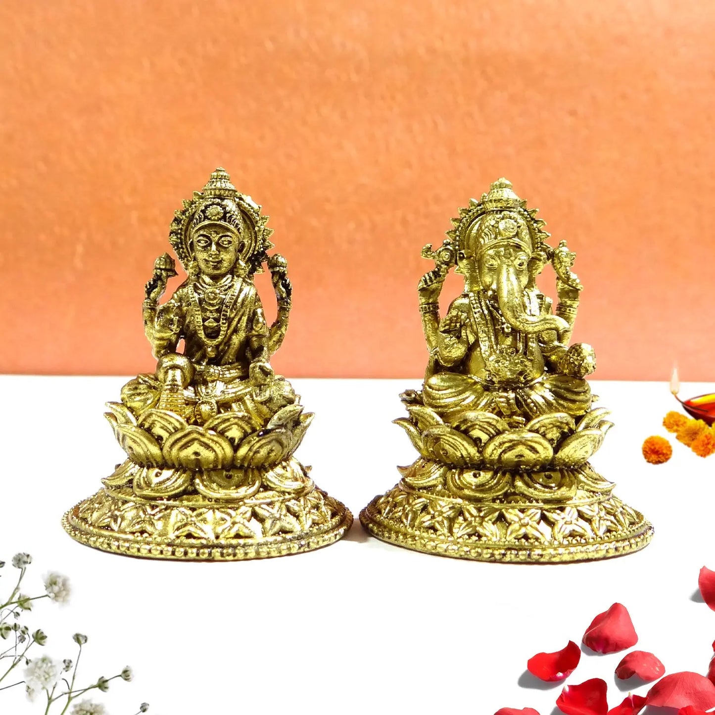 Two gold-colored deity statues on a white surface with an orange background