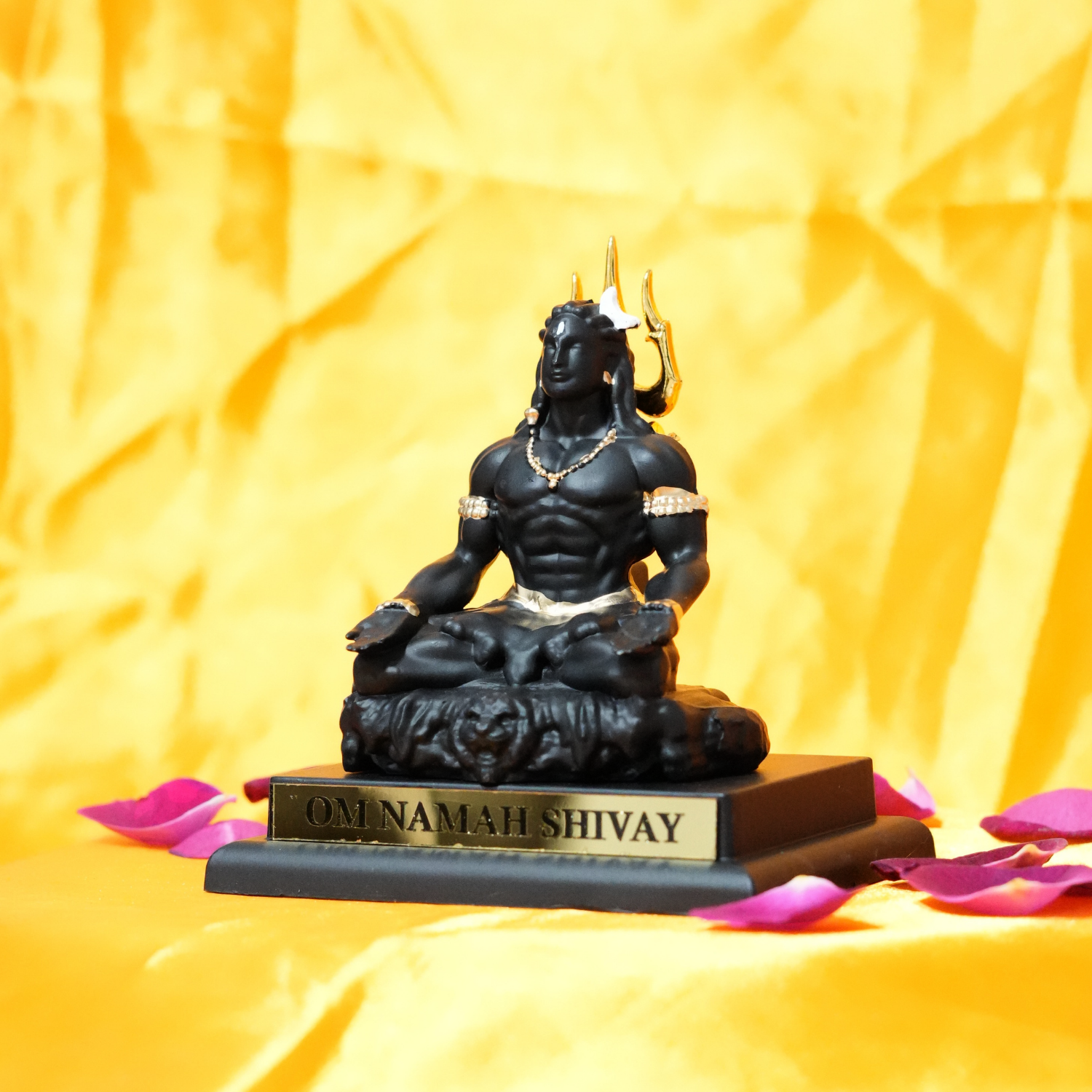 Black statue of a seated figure with 'OM NAMAH SHIVAY' on a yellow fabric background