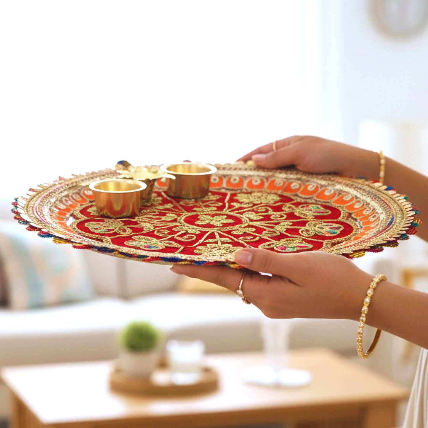 Decorative tray with gold coasters held by a hand in a living room setting
