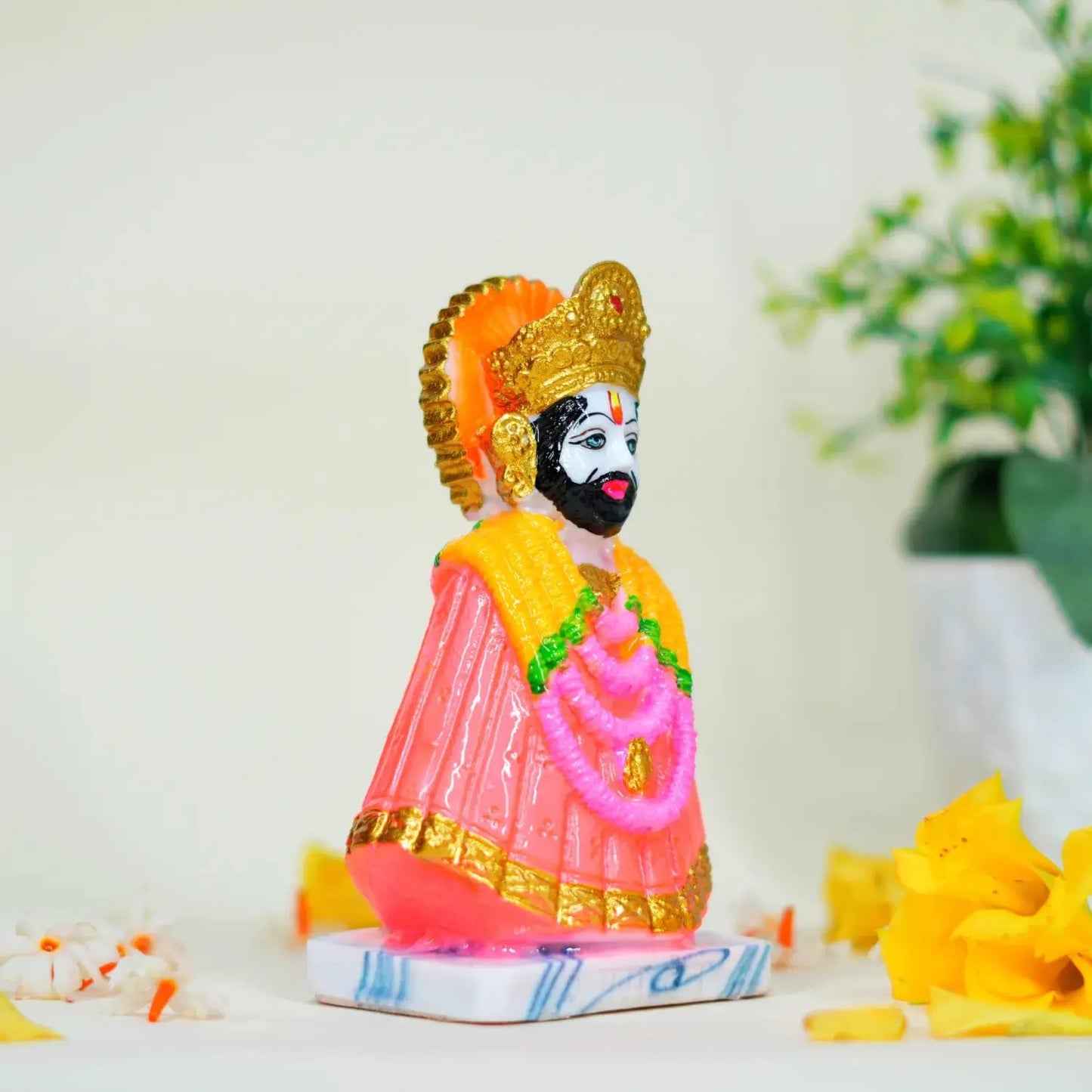 Colorful figurine of a deity with flowers and a plant in the background