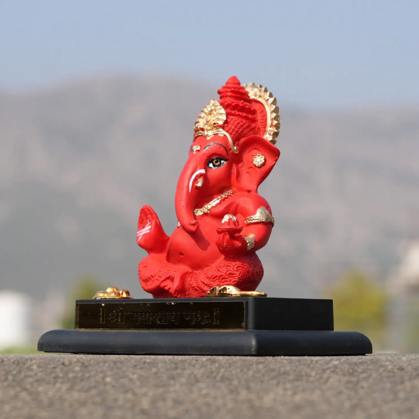 Red and gold Ganesh statue on a black base with a blurred natural background