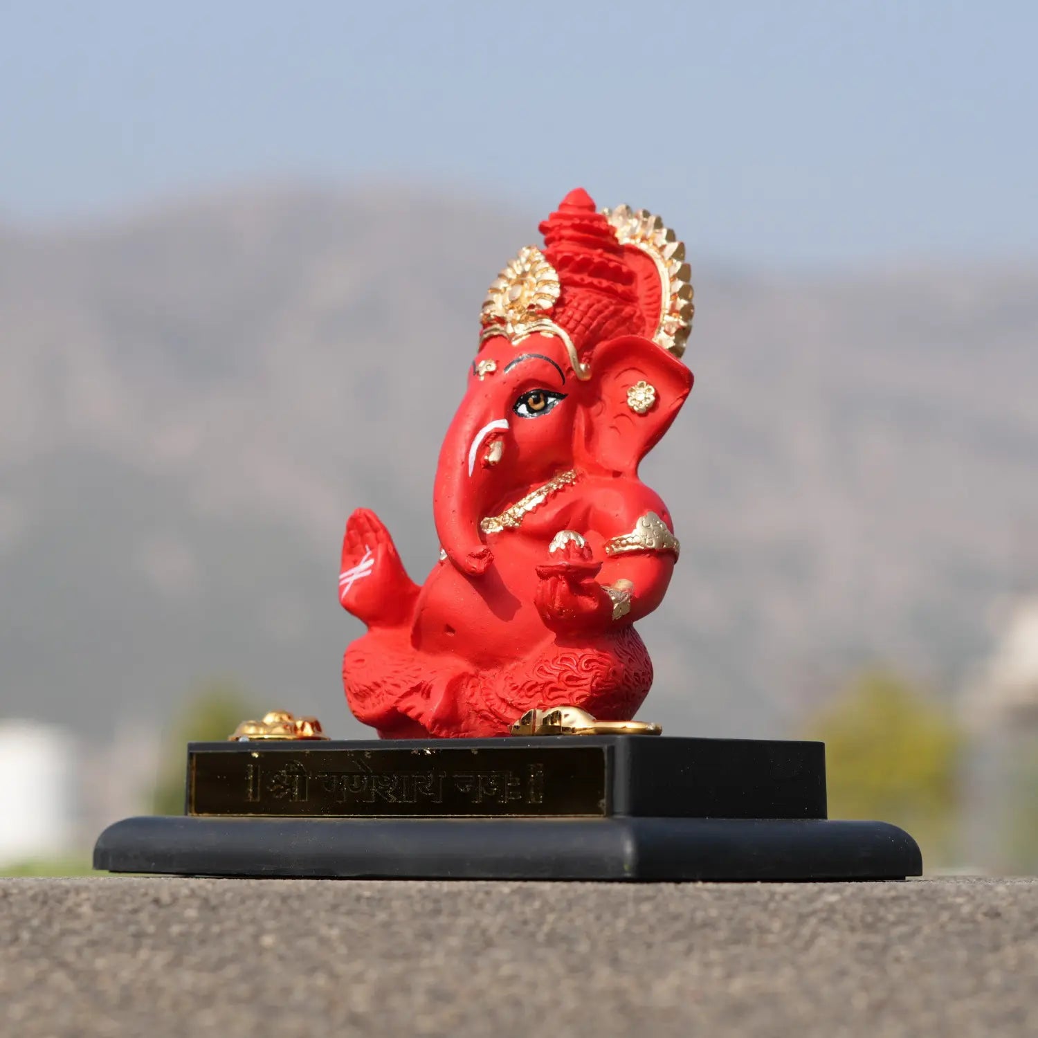 Red and gold Ganesh statue on a black base with a blurred natural background