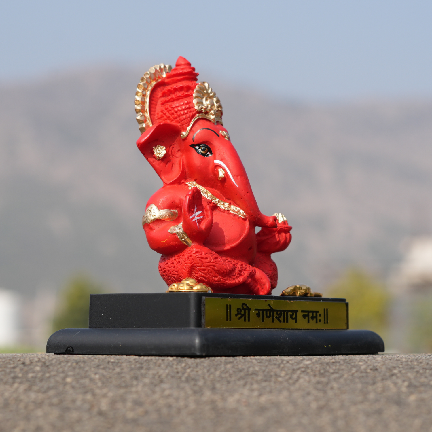 Red and gold Ganesh statue on a black base with a blurred natural background