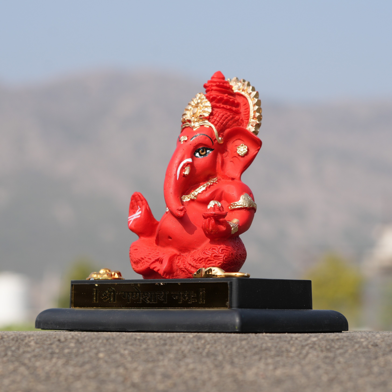 Red and gold Ganesh statue on a black base with a blurred natural background