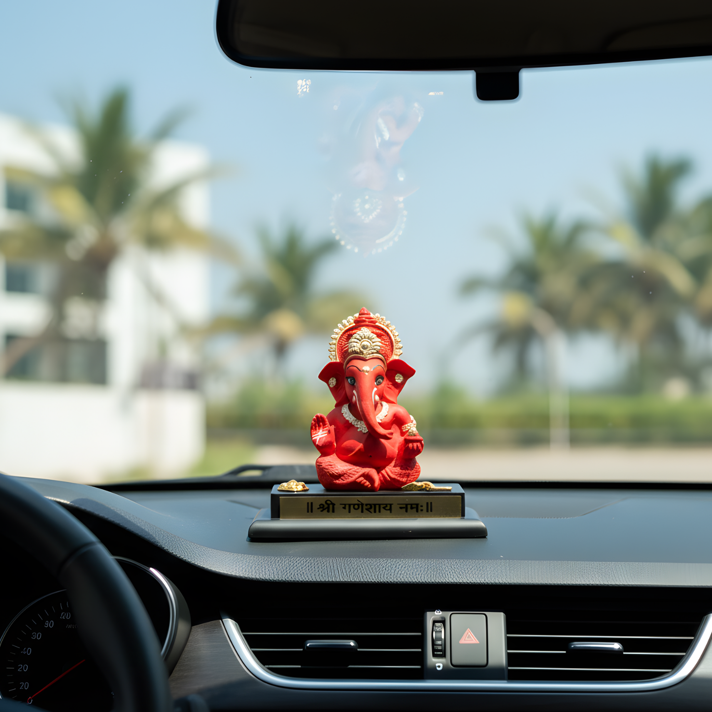 Red deity statue on a car dashboard with palm trees in the background