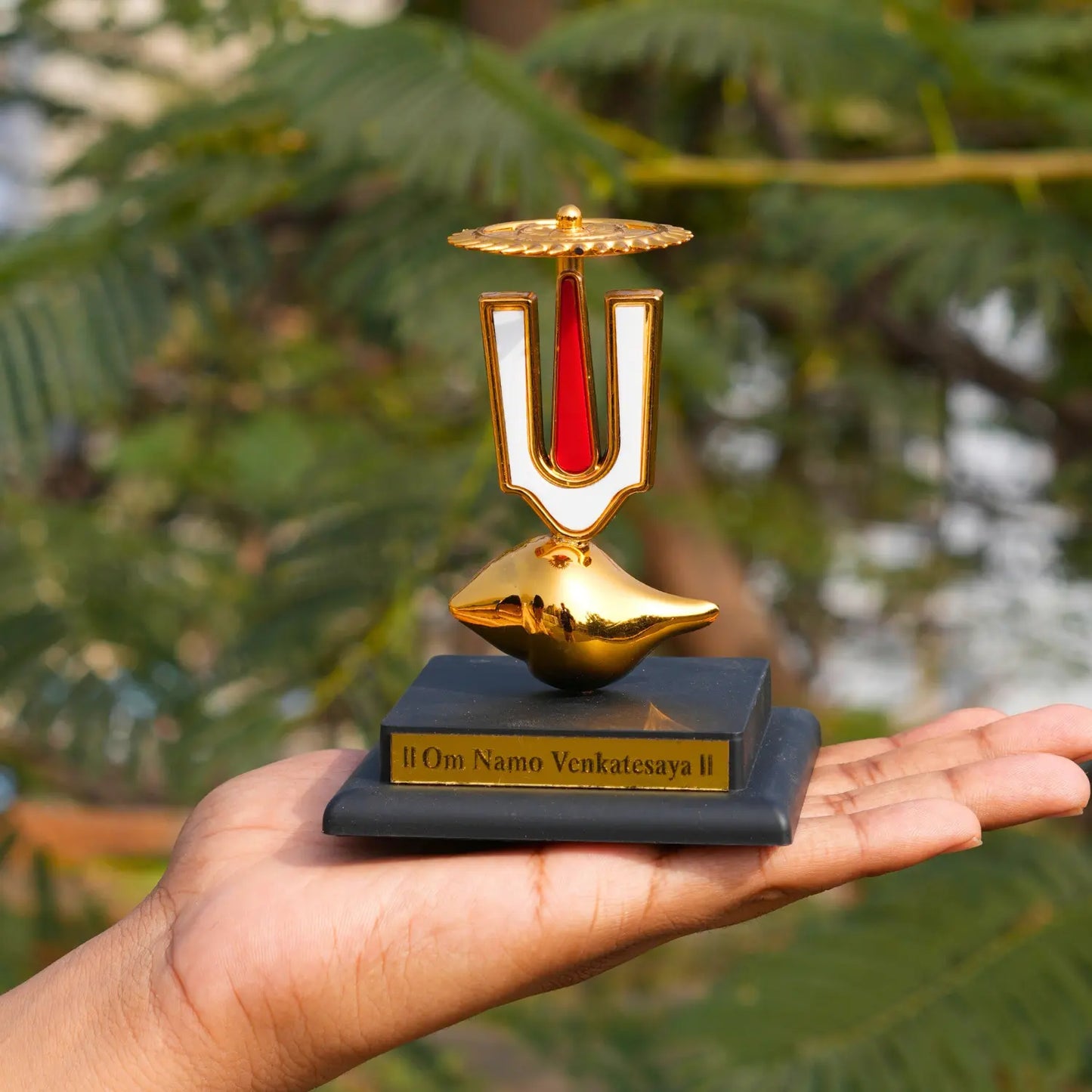 Gold and black decorative item held in a hand with a blurred green background