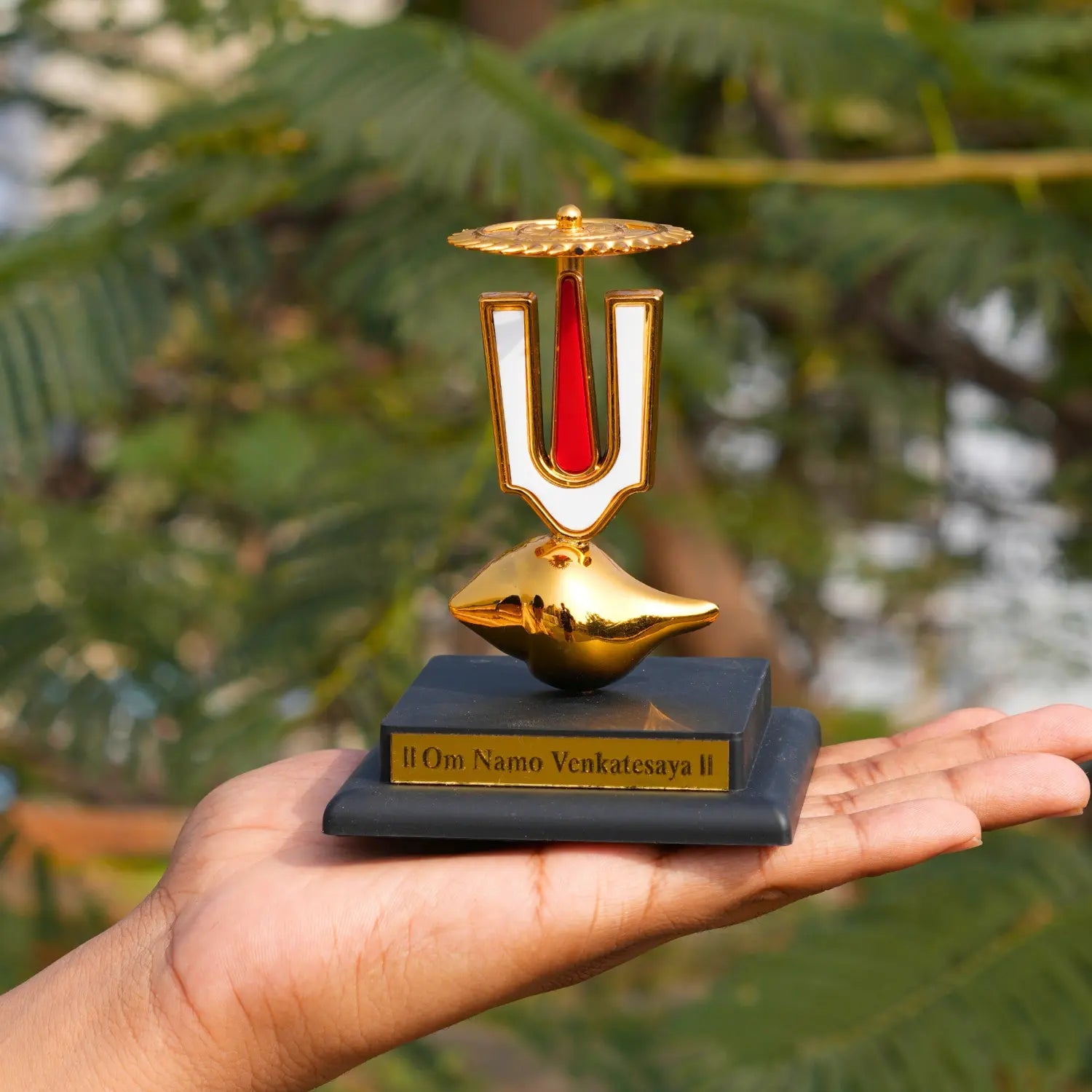 Gold and black decorative item held in a hand with a blurred green background