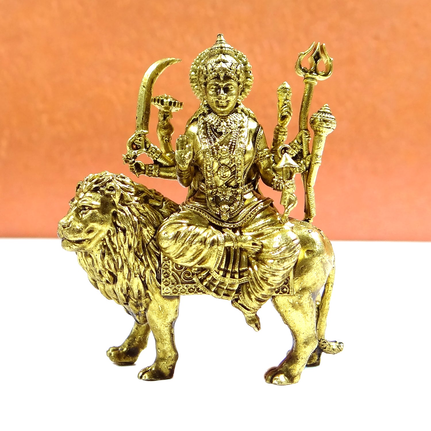 Gold-colored statue of a deity on a lion with a peach background