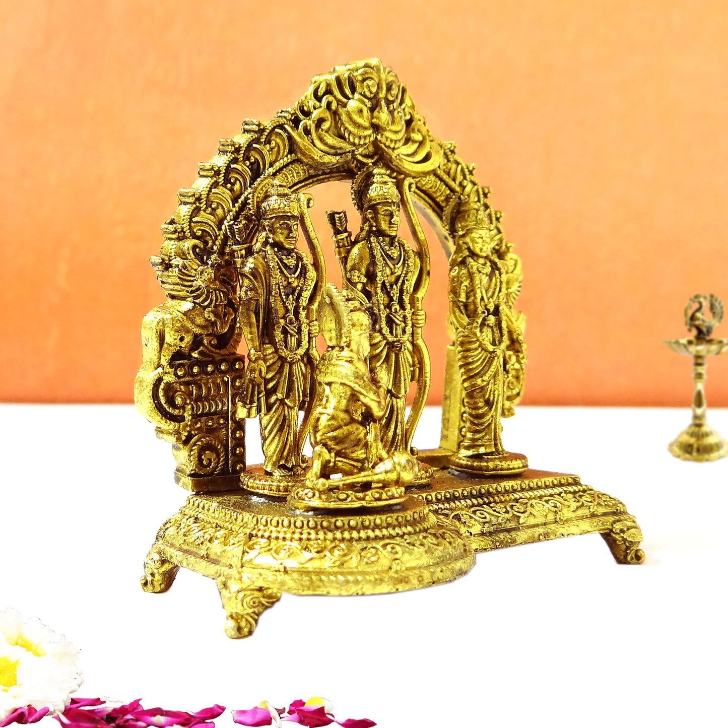 Decorative gold statue of three figures on a white surface with an orange background