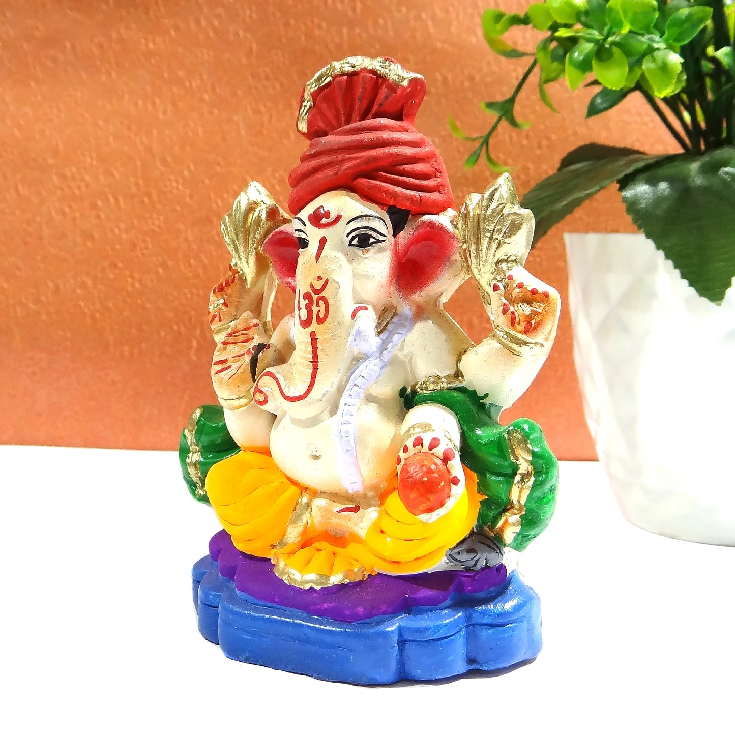 Colorful Ganesha statue with a red turban on a white surface.
