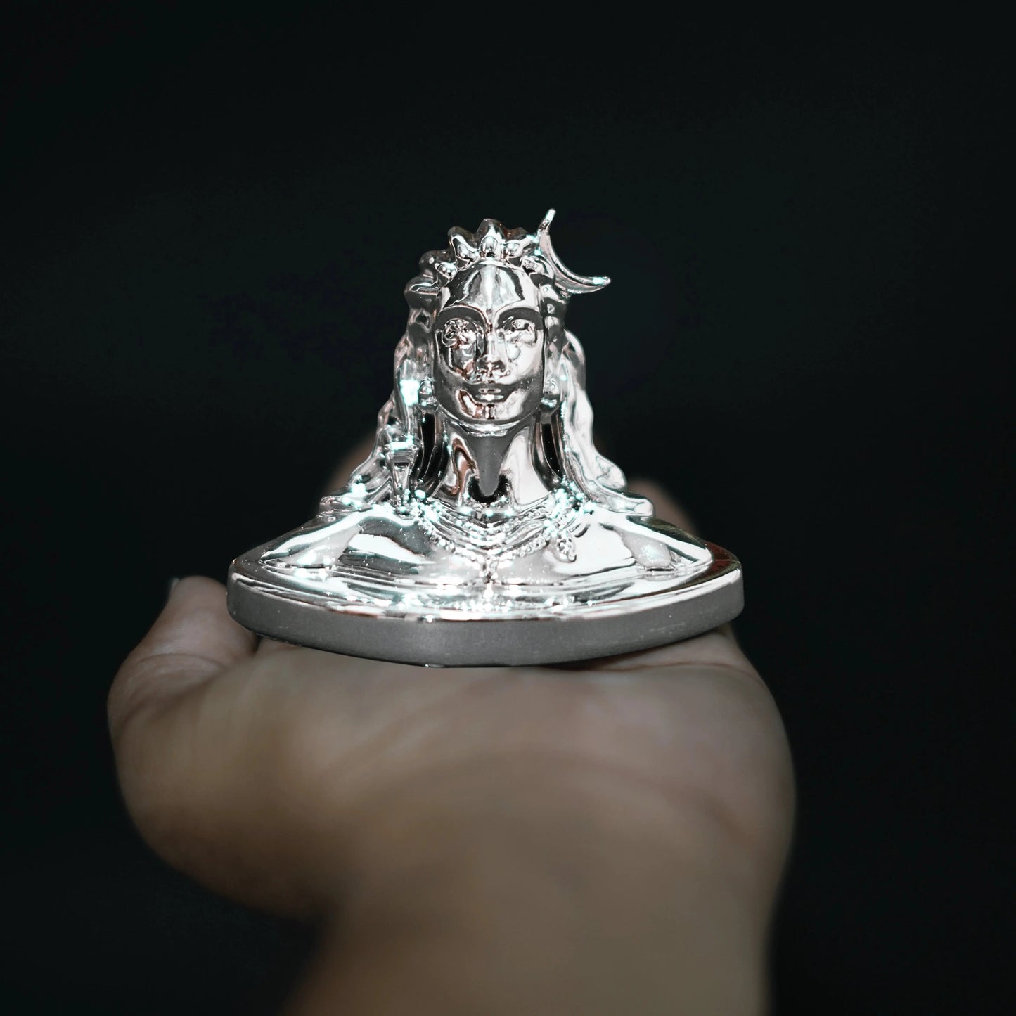 Silver statue held in a hand against a black background