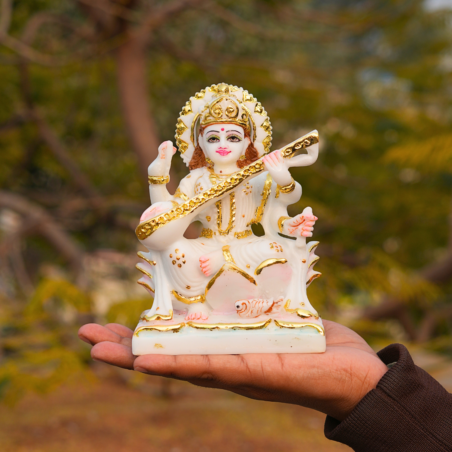 Small statue of a deity held in a hand with a blurred natural background