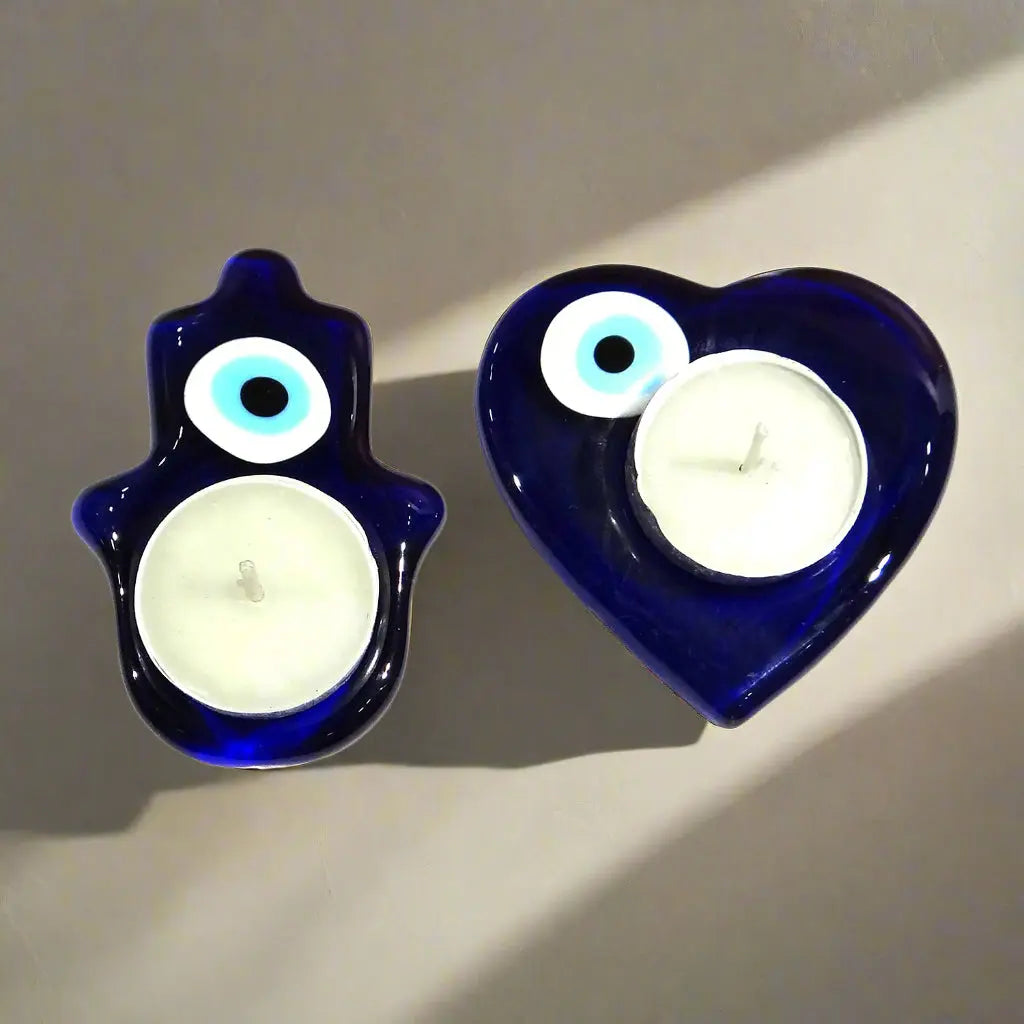 Two blue candle holders, one shaped like a hand and the other like a heart, with white candles inside on a white background.