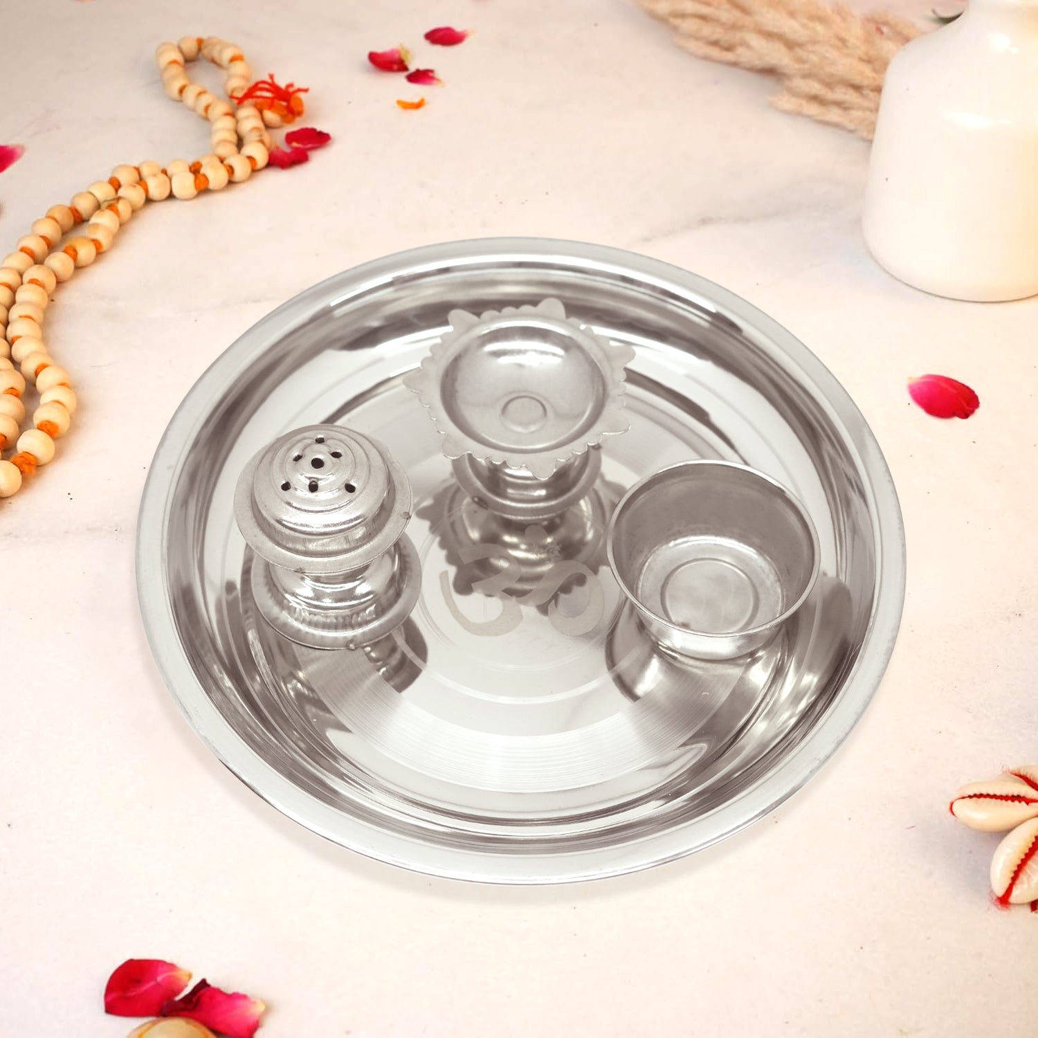 Stainless steel thali with three compartments on a light surface with decorative elements.
