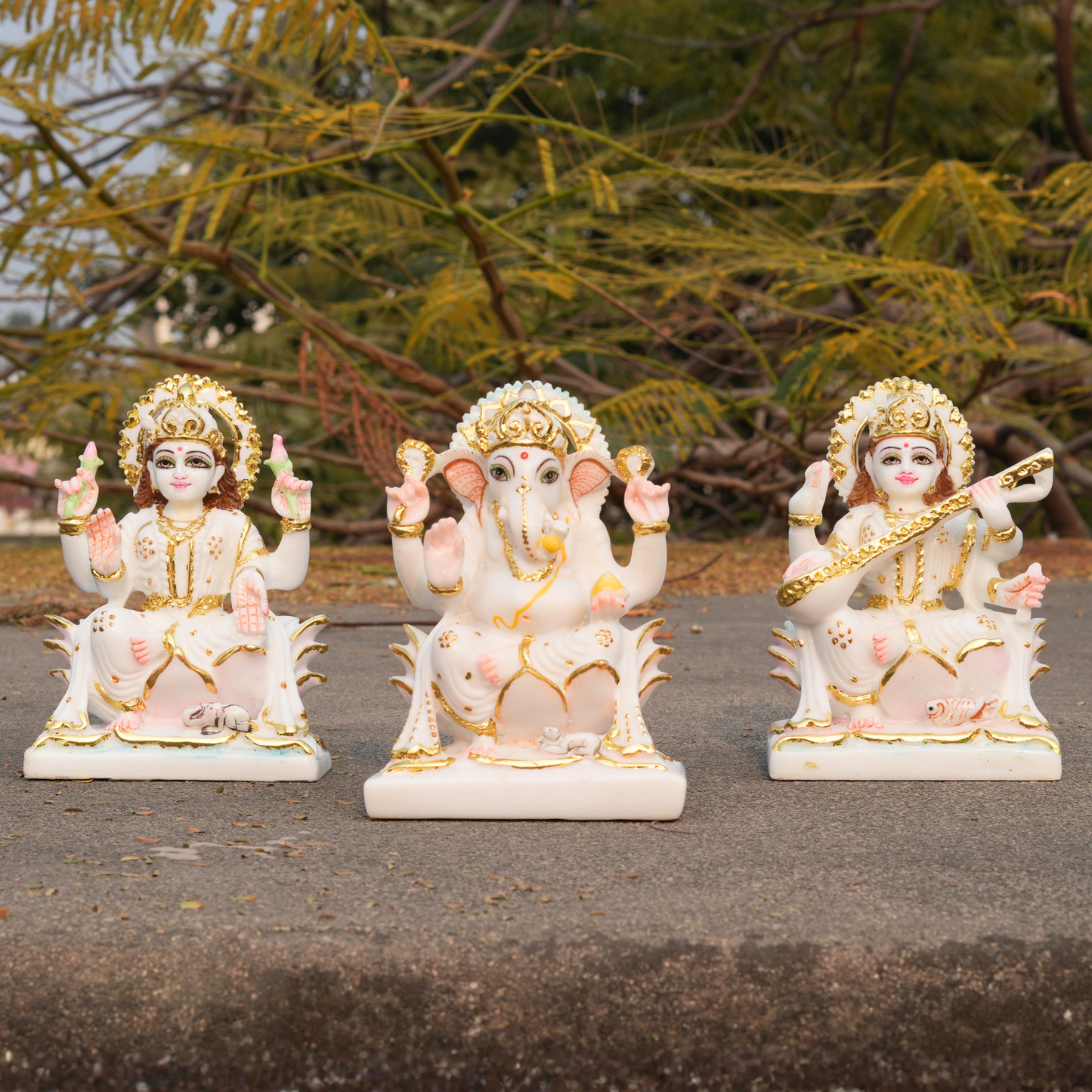 Three decorative statues of Hindu deities on a stone surface with greenery in the background.