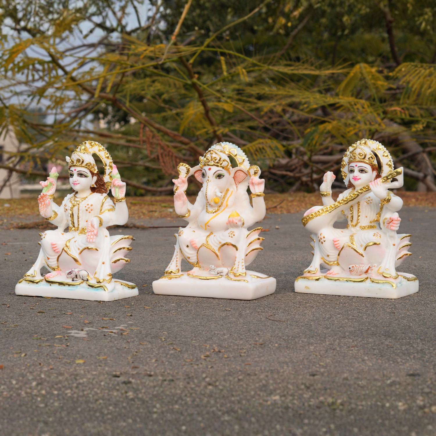 Three decorative statues of deities on a paved surface with greenery in the background