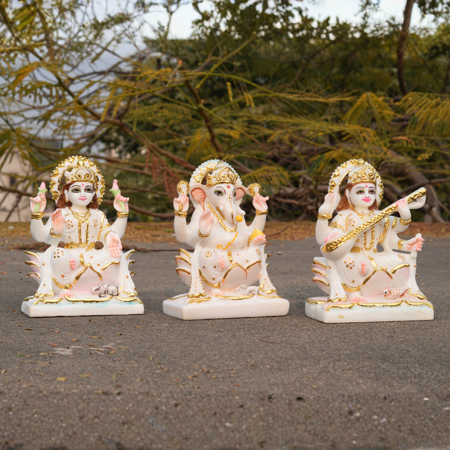 Three decorative statues of deities on a paved surface with greenery in the background