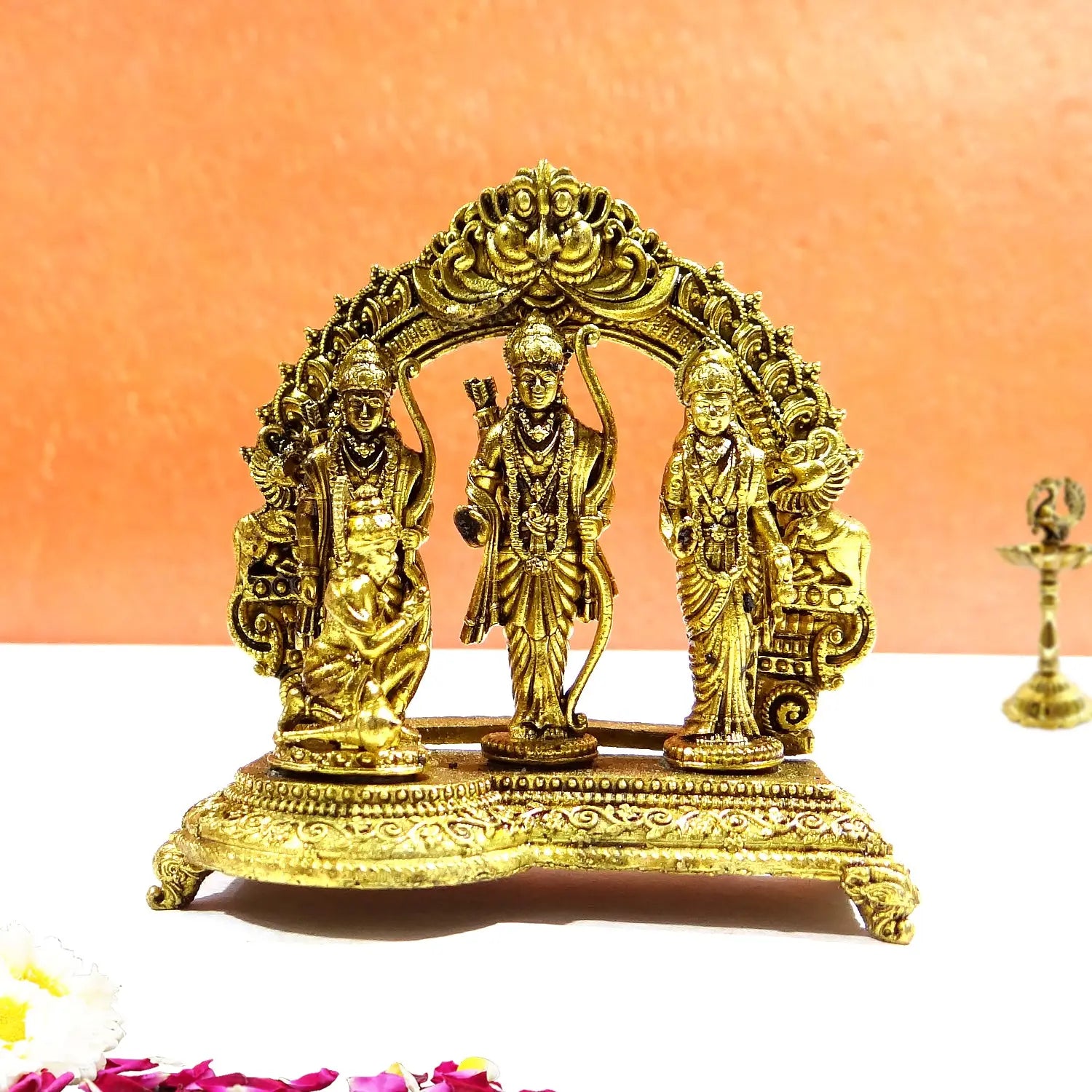 Decorative gold statue of three figures on a white surface with an orange background