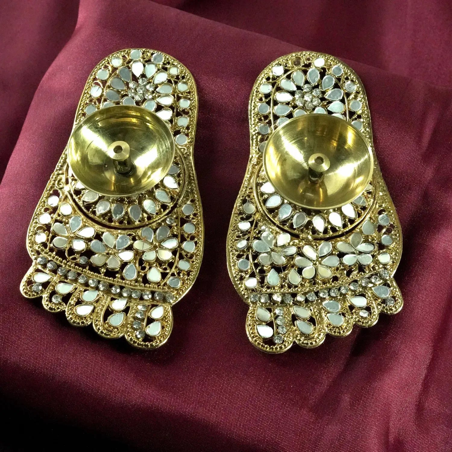 Pair of gold earrings with intricate designs on a maroon fabric background
