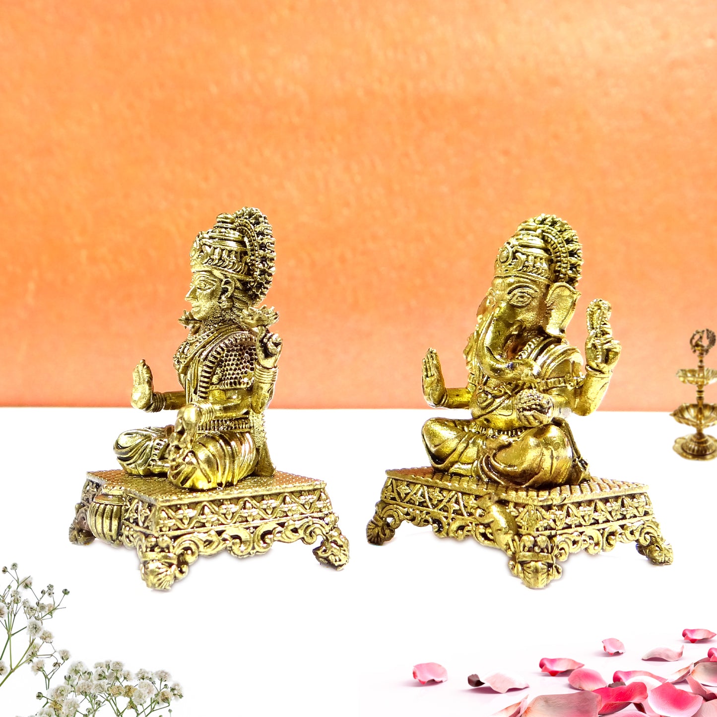 Two gold-colored statues on a peach background with flowers and petals at the bottom.