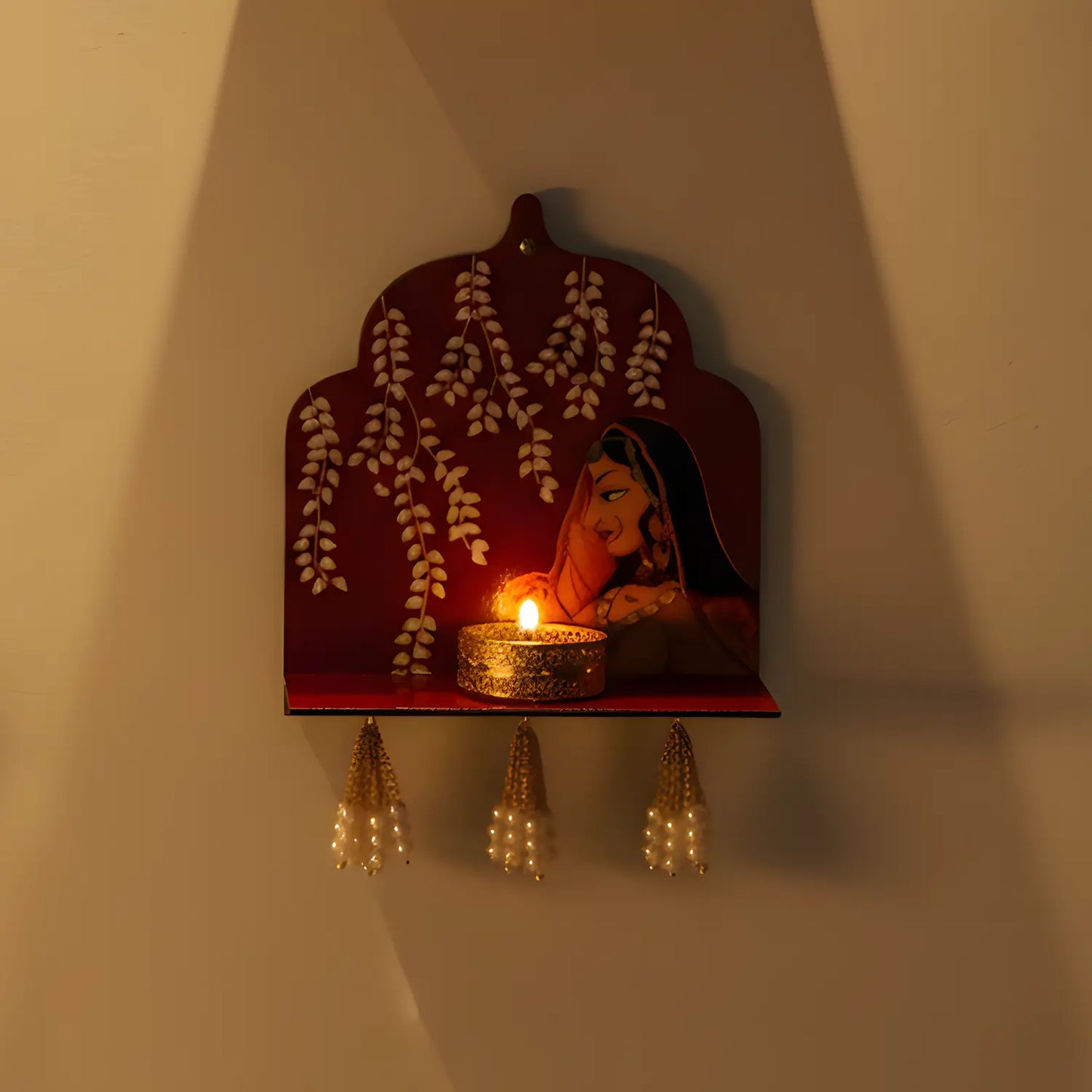 Decorative wall shelf with a lit candle and floral design on a plain wall.