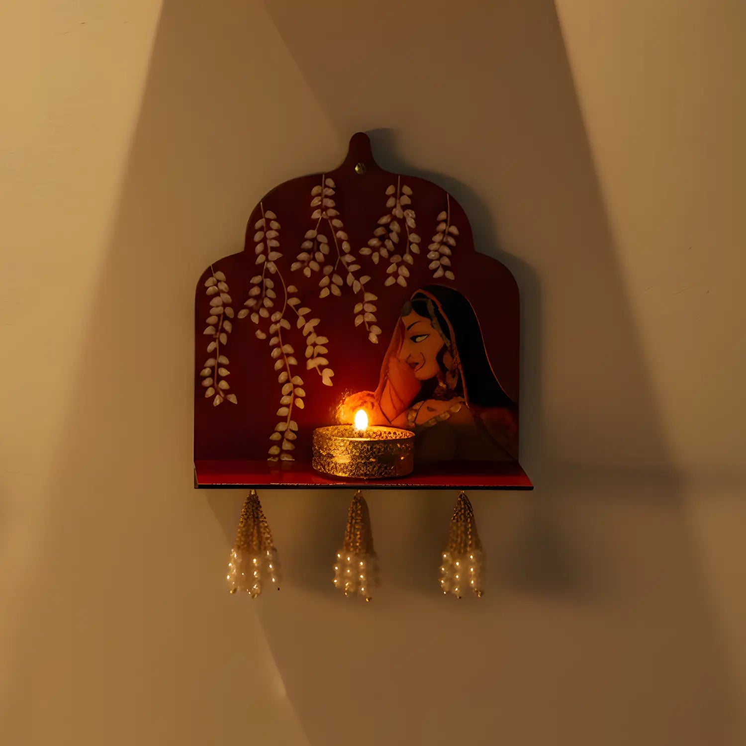 Decorative wall shelf with a lit candle and floral design on a plain wall.
