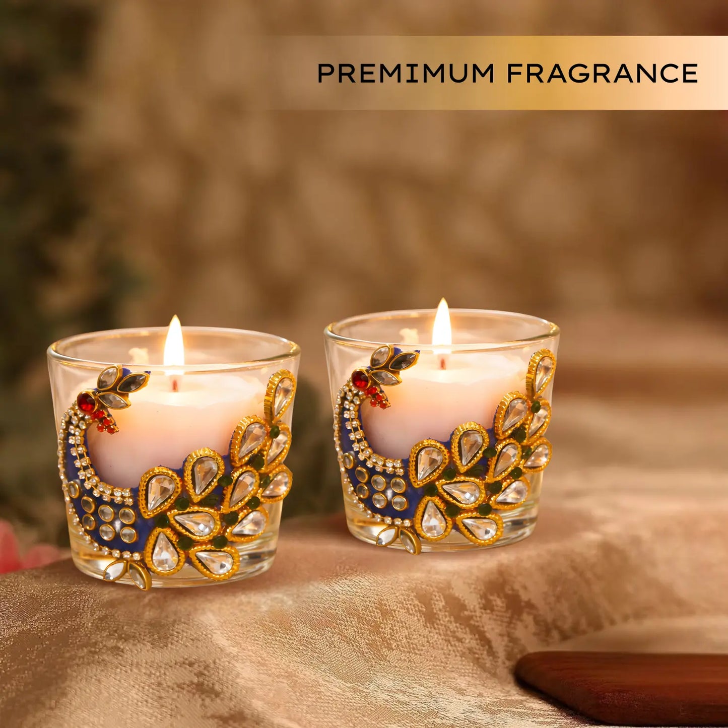 Two decorative candles in glass holders with intricate designs on a soft fabric background, labeled 'Premium Fragrance'.
