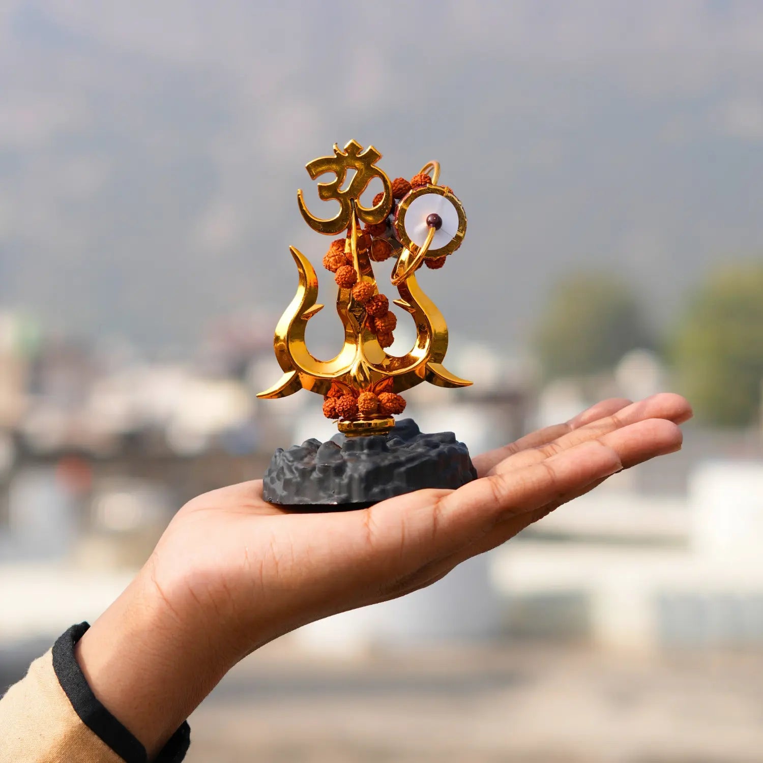 Hand holding a small decorative object with gold and orange elements against a blurred background