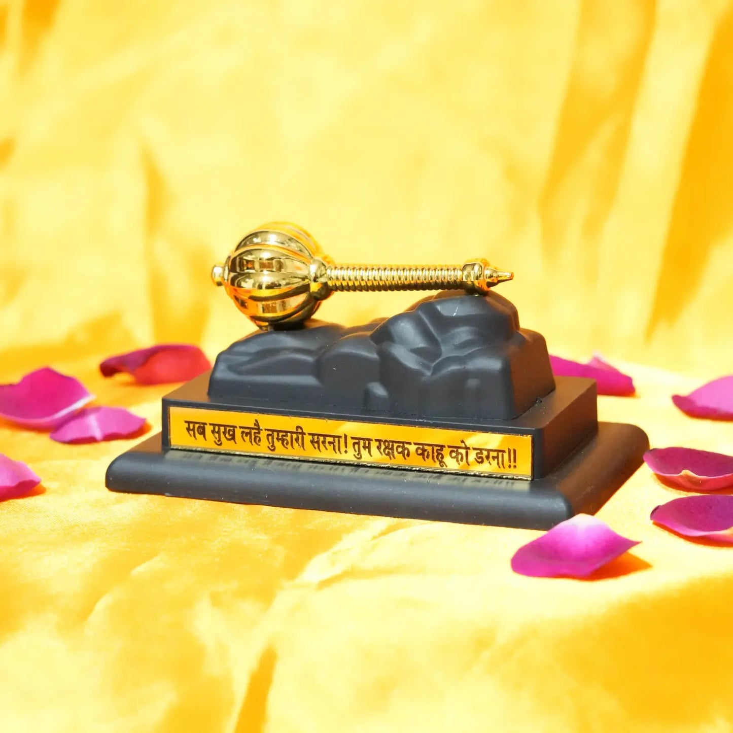 Decorative item with gold key on a black base on a yellow background with pink petals.