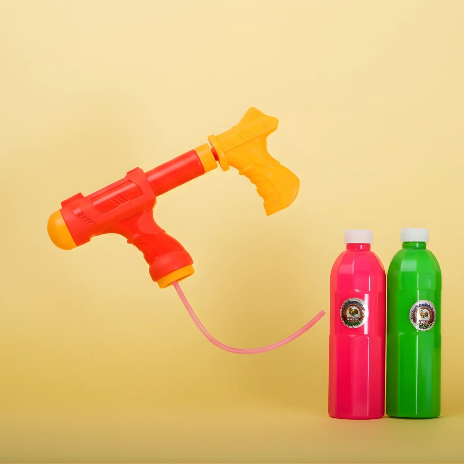 Red and yellow water gun with pink hose and two colorful bottles on a yellow background