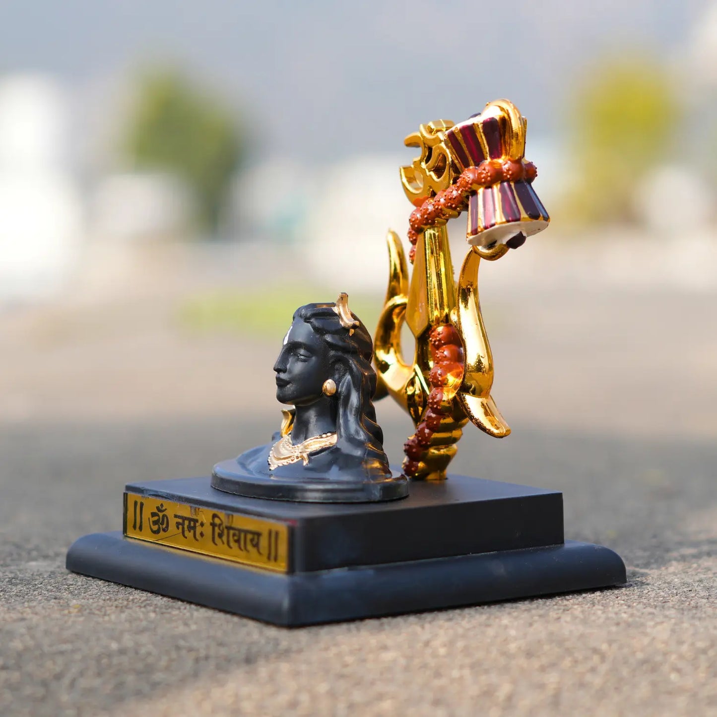 Decorative statue with a black base, gold and red elements, and a blurred outdoor background.