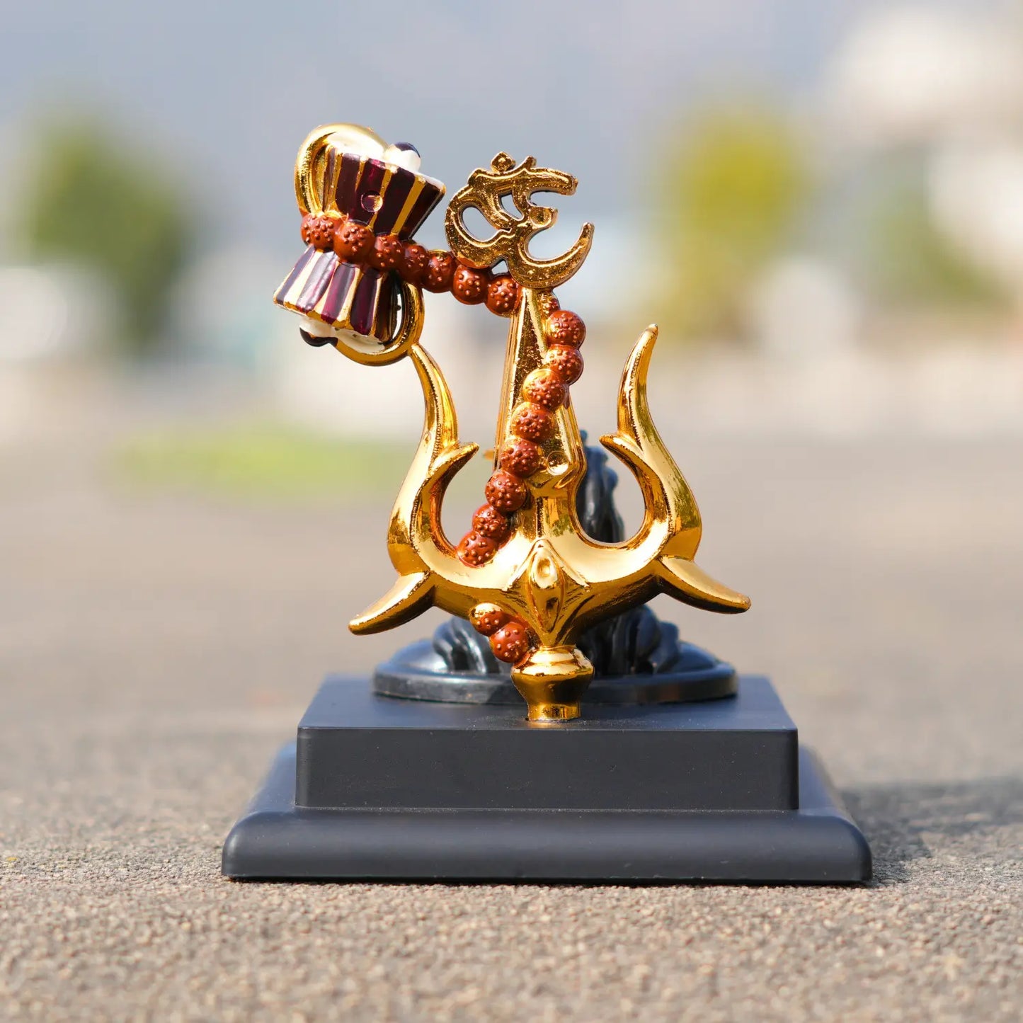 Decorative item with gold and red elements on a gray base against a blurred outdoor background
