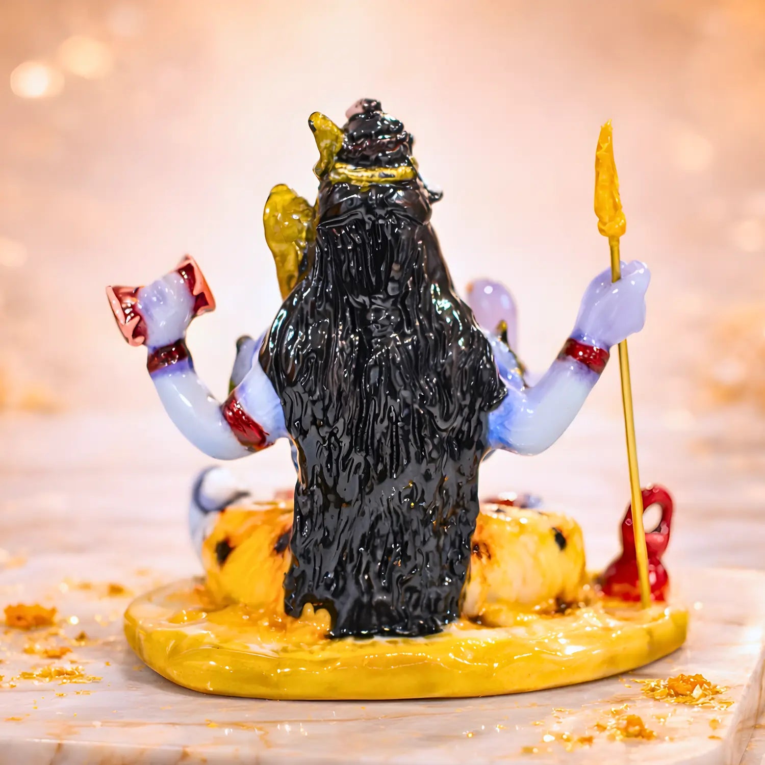 Statue of a multi-armed deity with a yellow crown and staff on a marble surface.