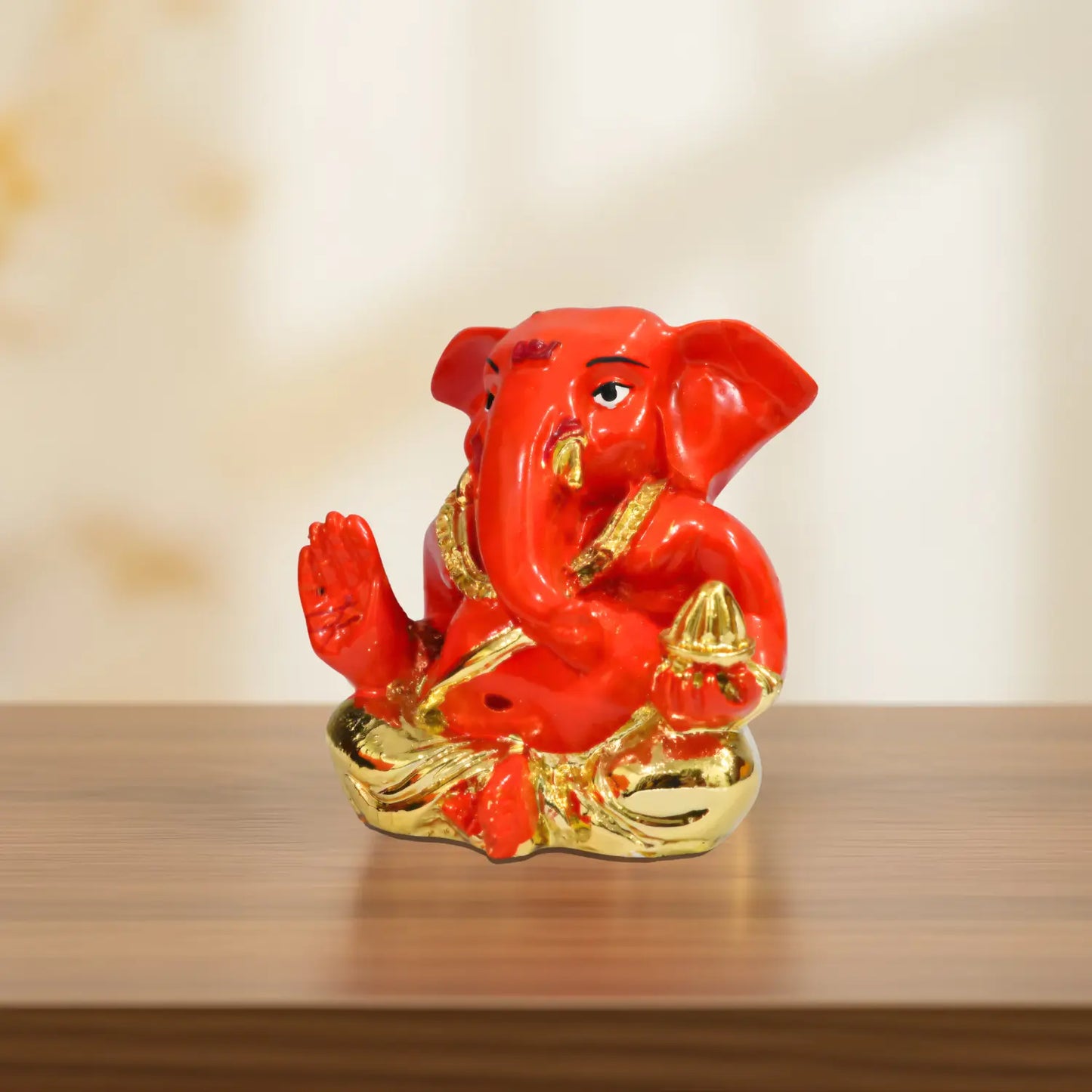Red and gold Ganesha statue on a wooden surface with a blurred background