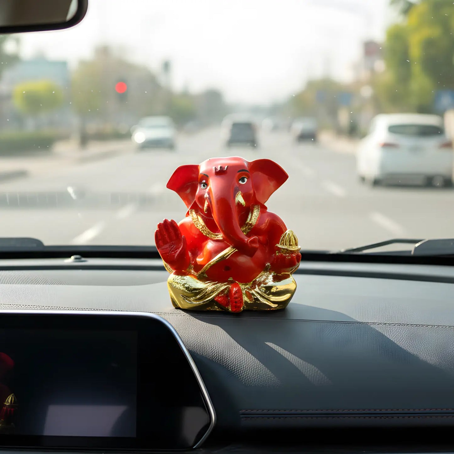 Red and gold figurine of a deity on a car dashboard with traffic in the background