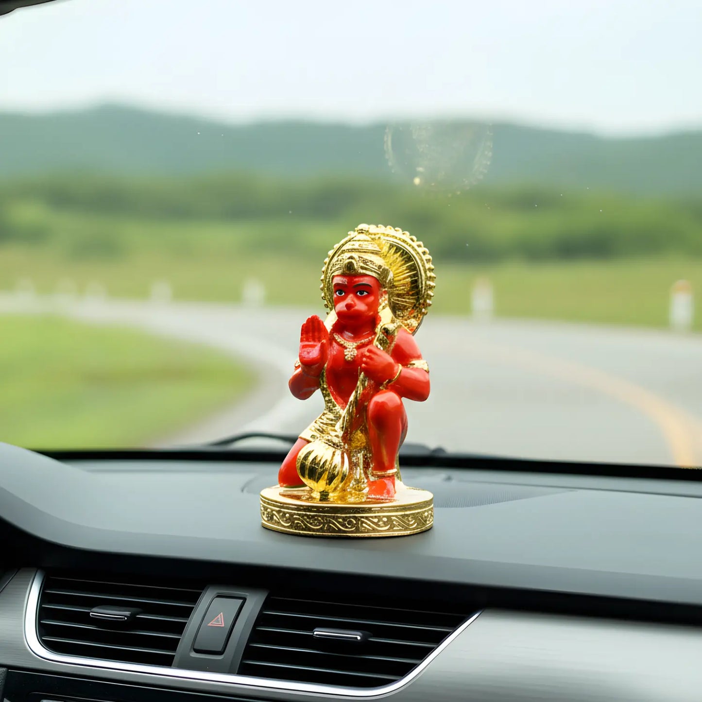 Decorative statue on a car dashboard with a scenic road in the background