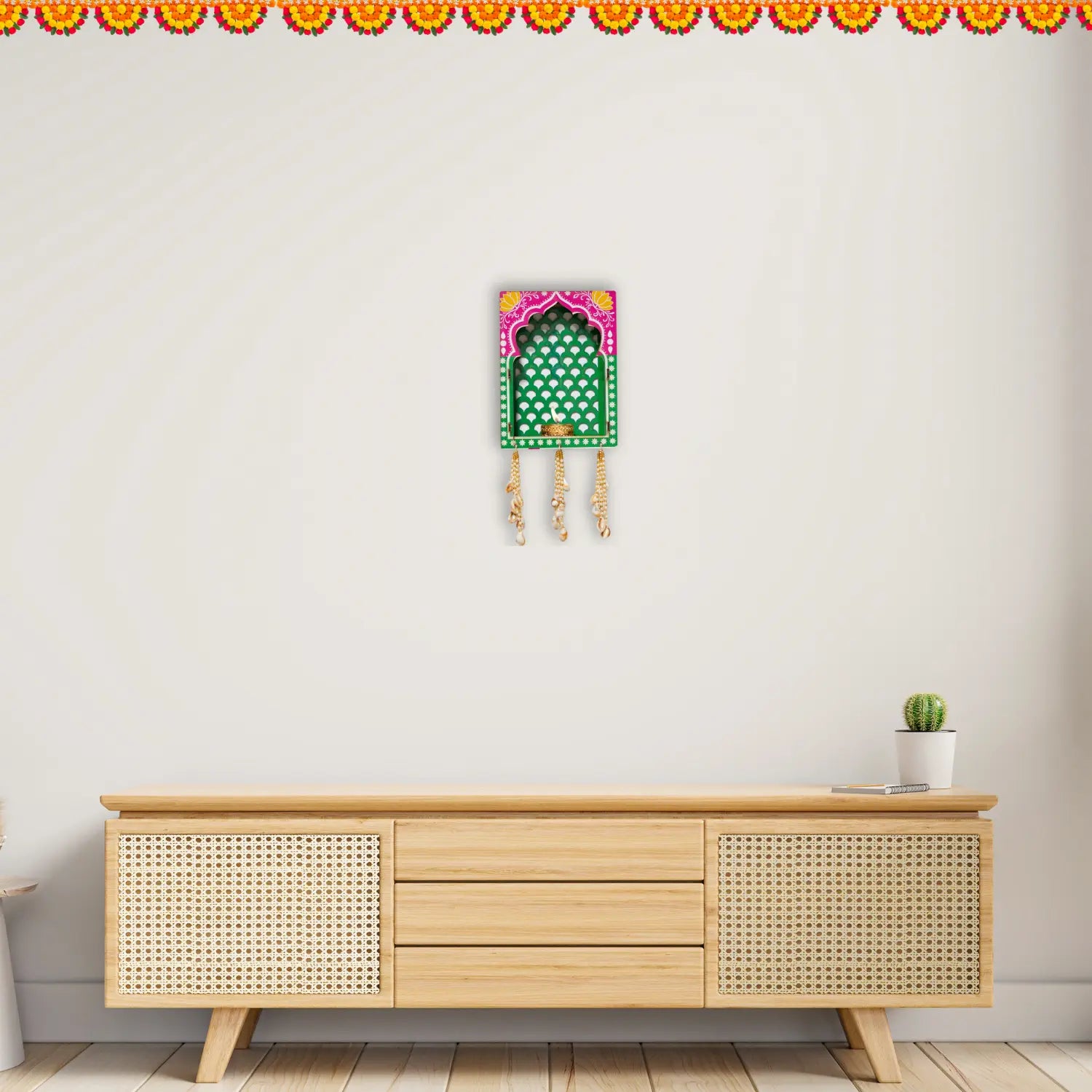 Decorative wall hanging above a wooden cabinet with a small plant on a white wall.