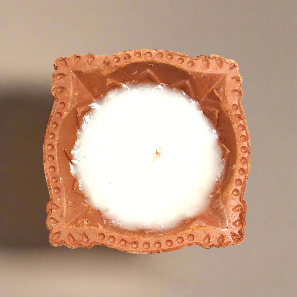 Terracotta square candle holder with a white candle inside on a white background
