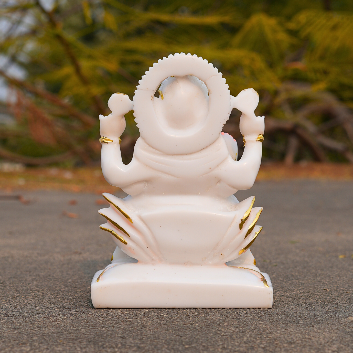 White marble statue of a deity with gold accents on a blurred natural background