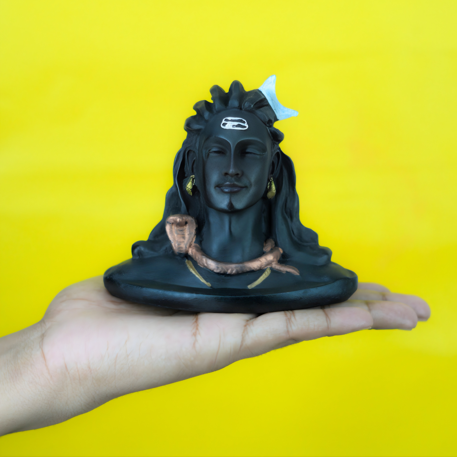 Black figurine of a stylized face held in a hand against a yellow background