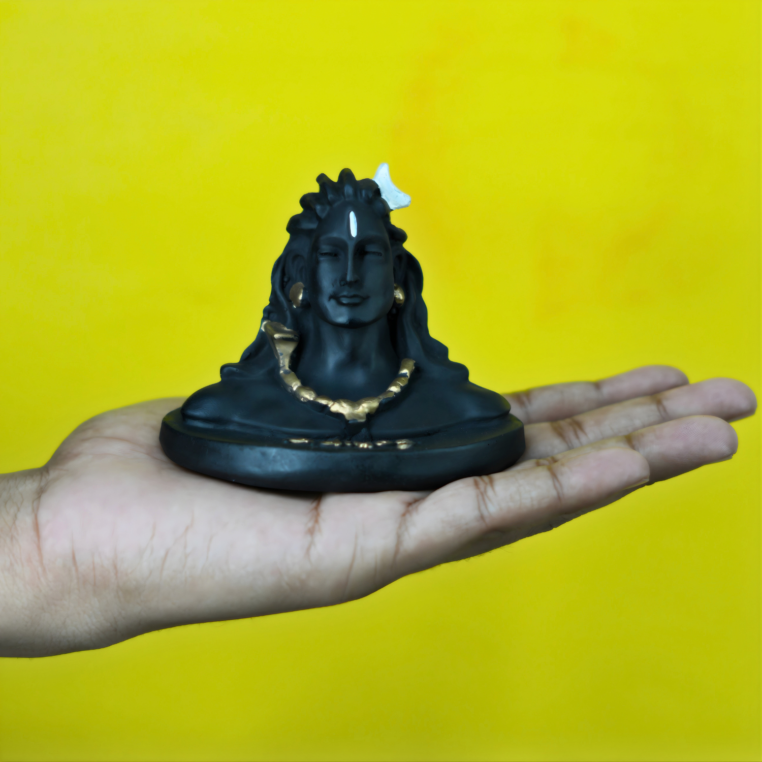Black Shiva statue held in a hand against a yellow background