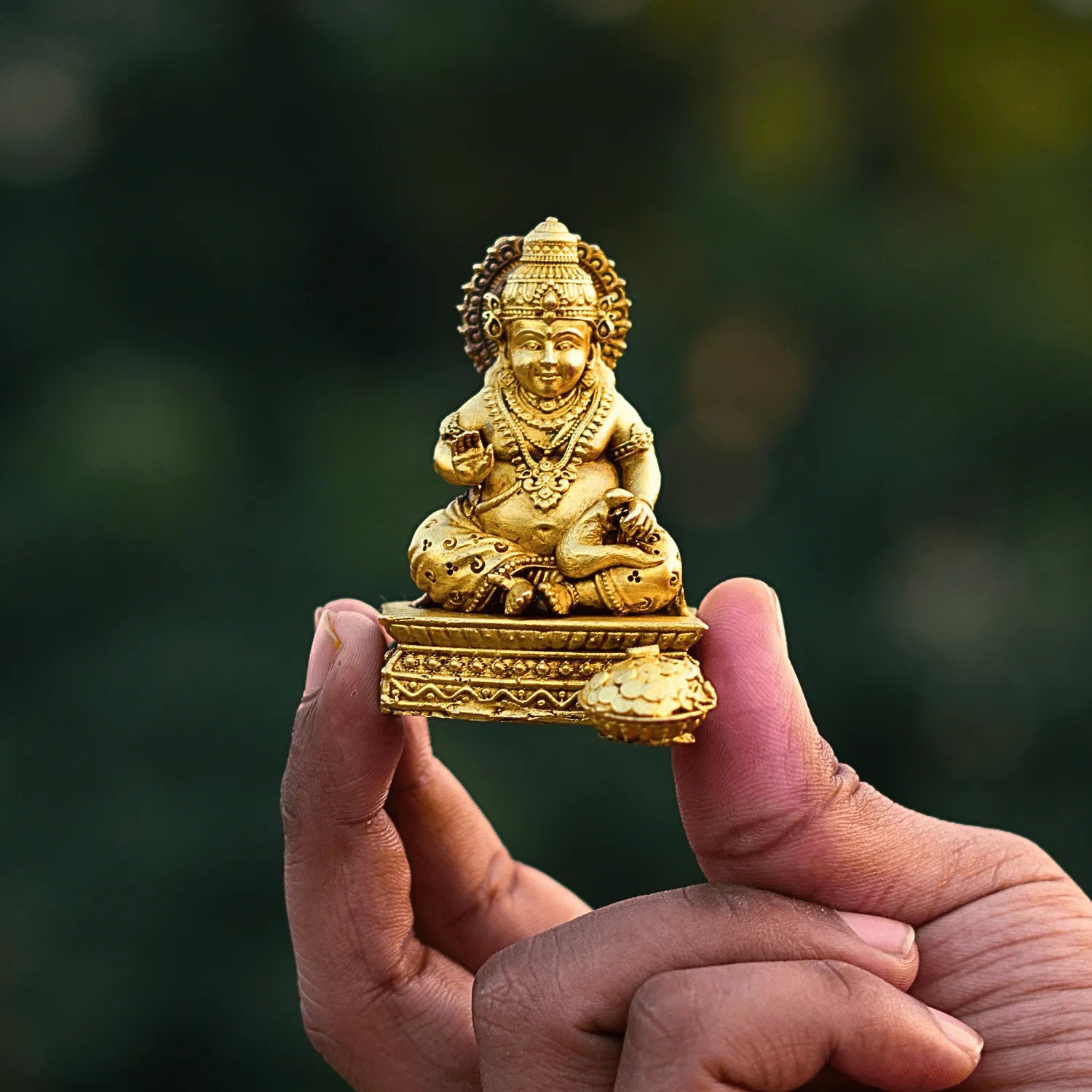 Gold-colored statue held in a hand with a blurred green background