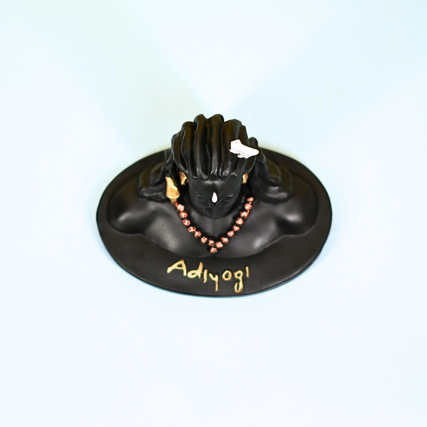Black sculpture of a hand with a necklace on a round base, branded 'Adiyogi', on a light blue background.