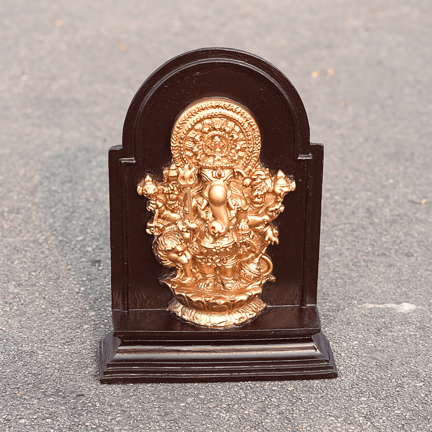 Gold-colored deity statue on a dark wooden base against a gray background