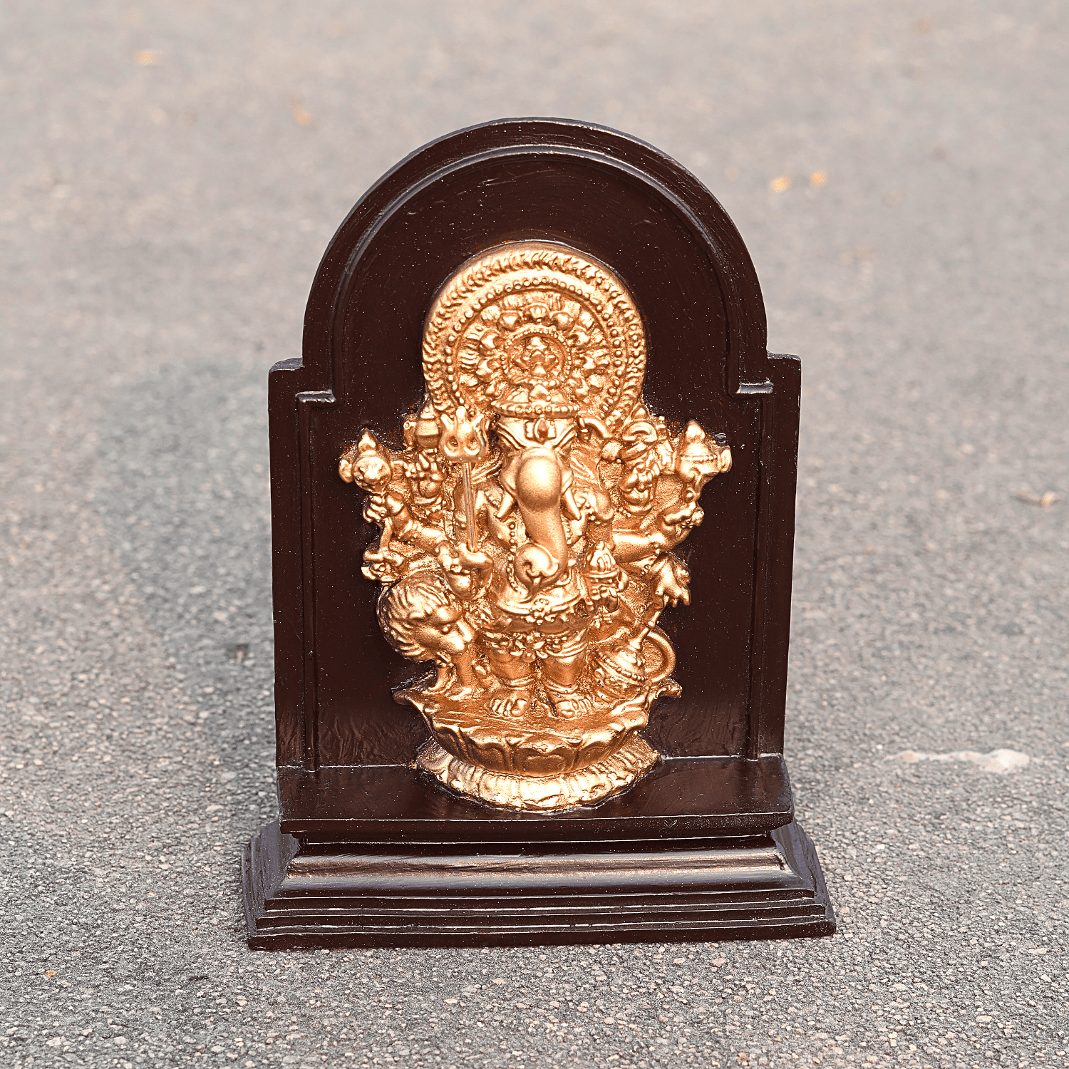 Gold-colored deity statue on a dark wooden base against a gray background