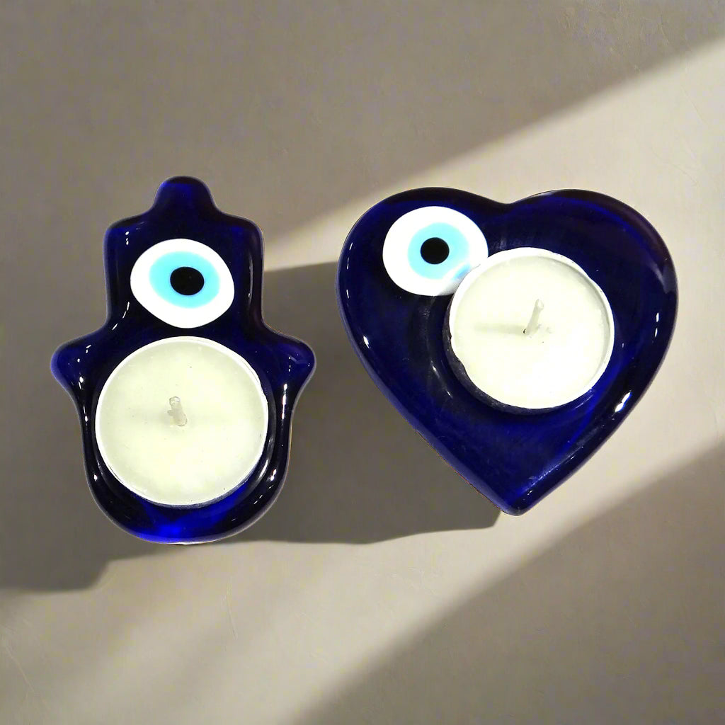 Two blue candle holders, one shaped like a hand and the other like a heart, with white candles inside on a white background.