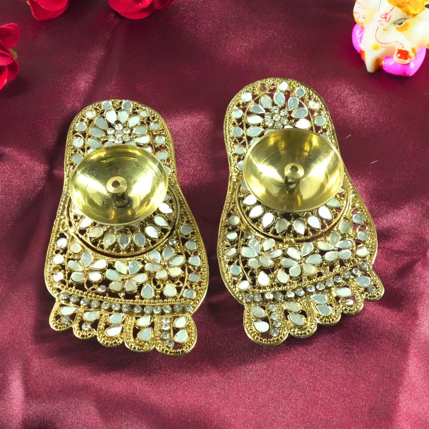 Pair of gold earrings with intricate designs on a maroon fabric background