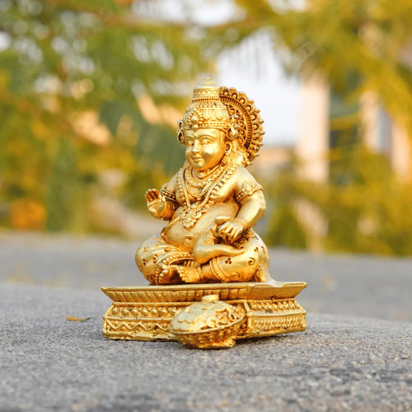 Gold-colored statue of a seated figure on a textured surface with blurred greenery in the background