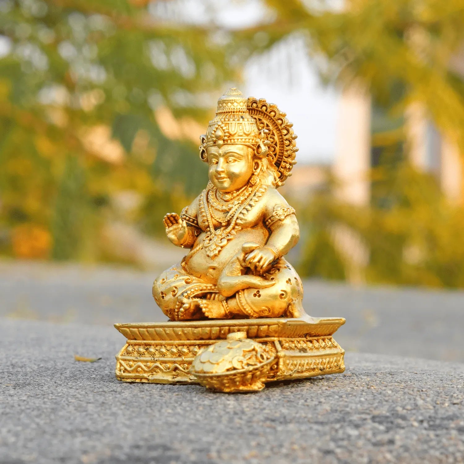 Gold-colored statue of a seated figure on a textured surface with blurred greenery in the background