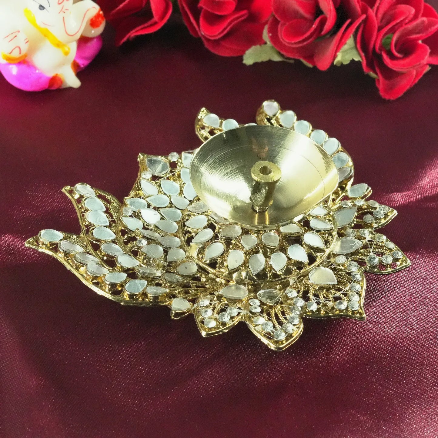 Decorative gold lotus-shaped diya with white stones on a red fabric background.